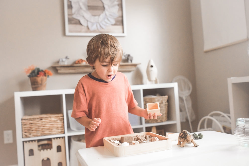 Un garçon en t-shirt orange à col rond se tient devant une table en bois blanc avec des cupcakes.