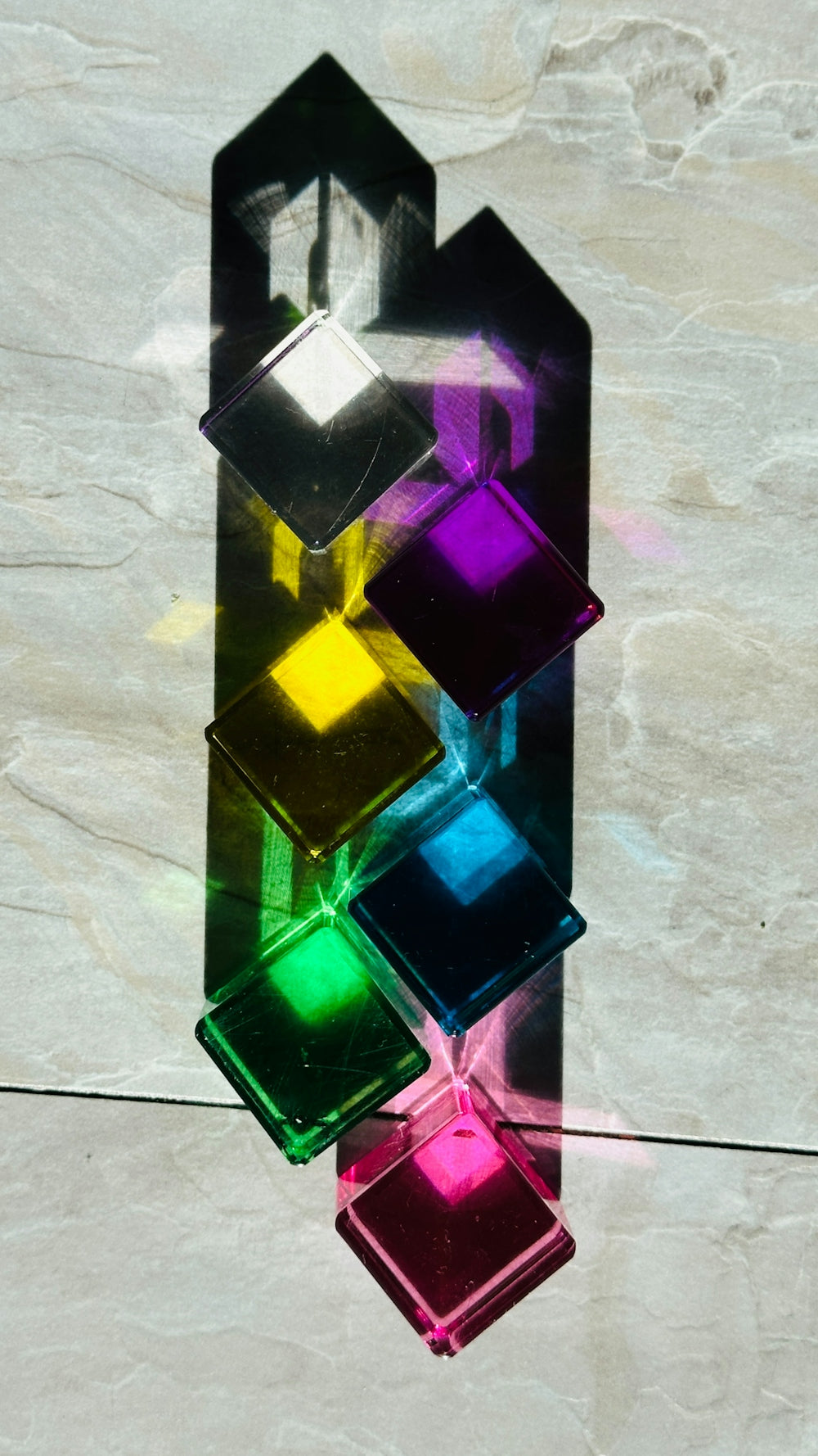 Colorful glass squares casting shadows on a textured surface.