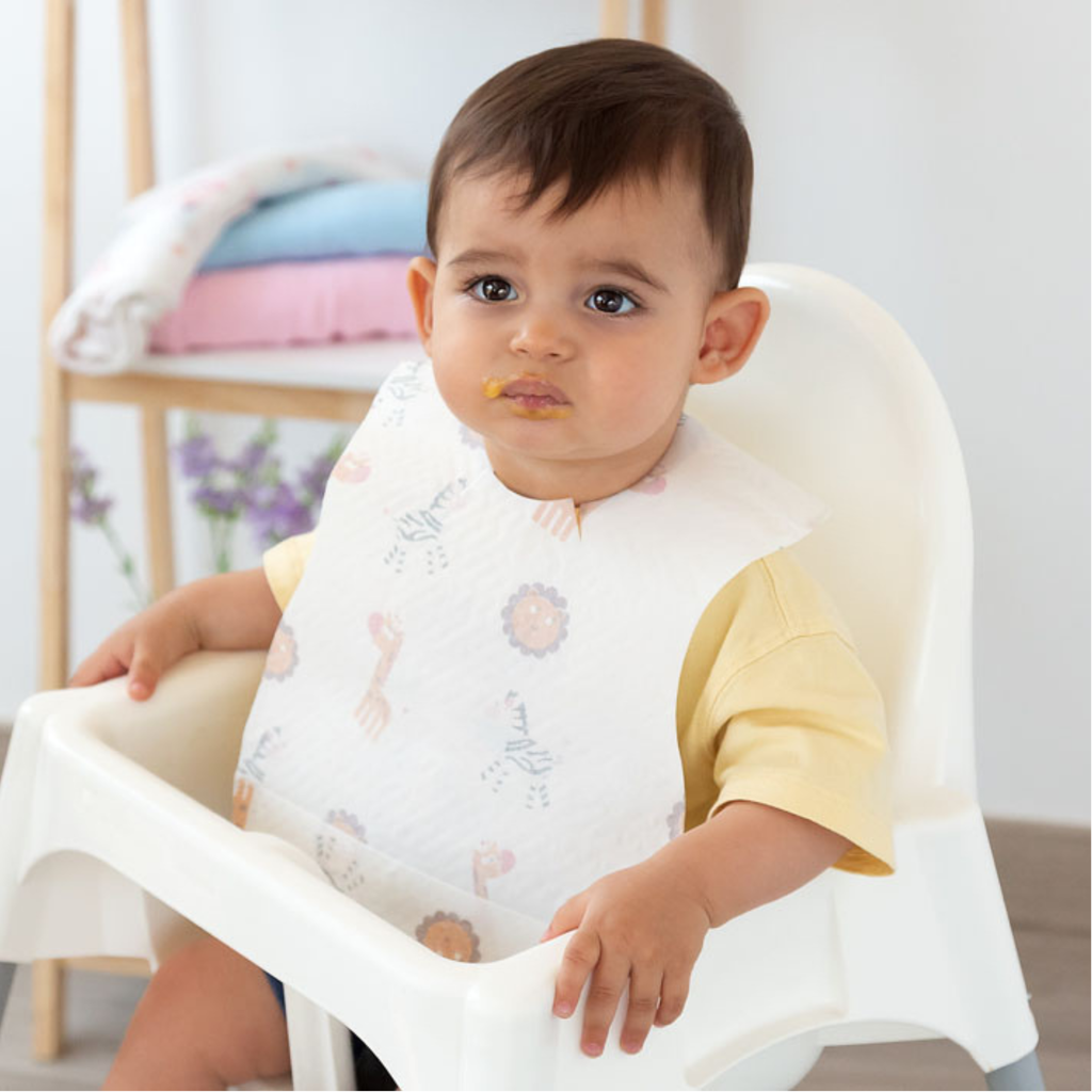 Bebé usando un babero desechable con estampado de animales durante la comida.