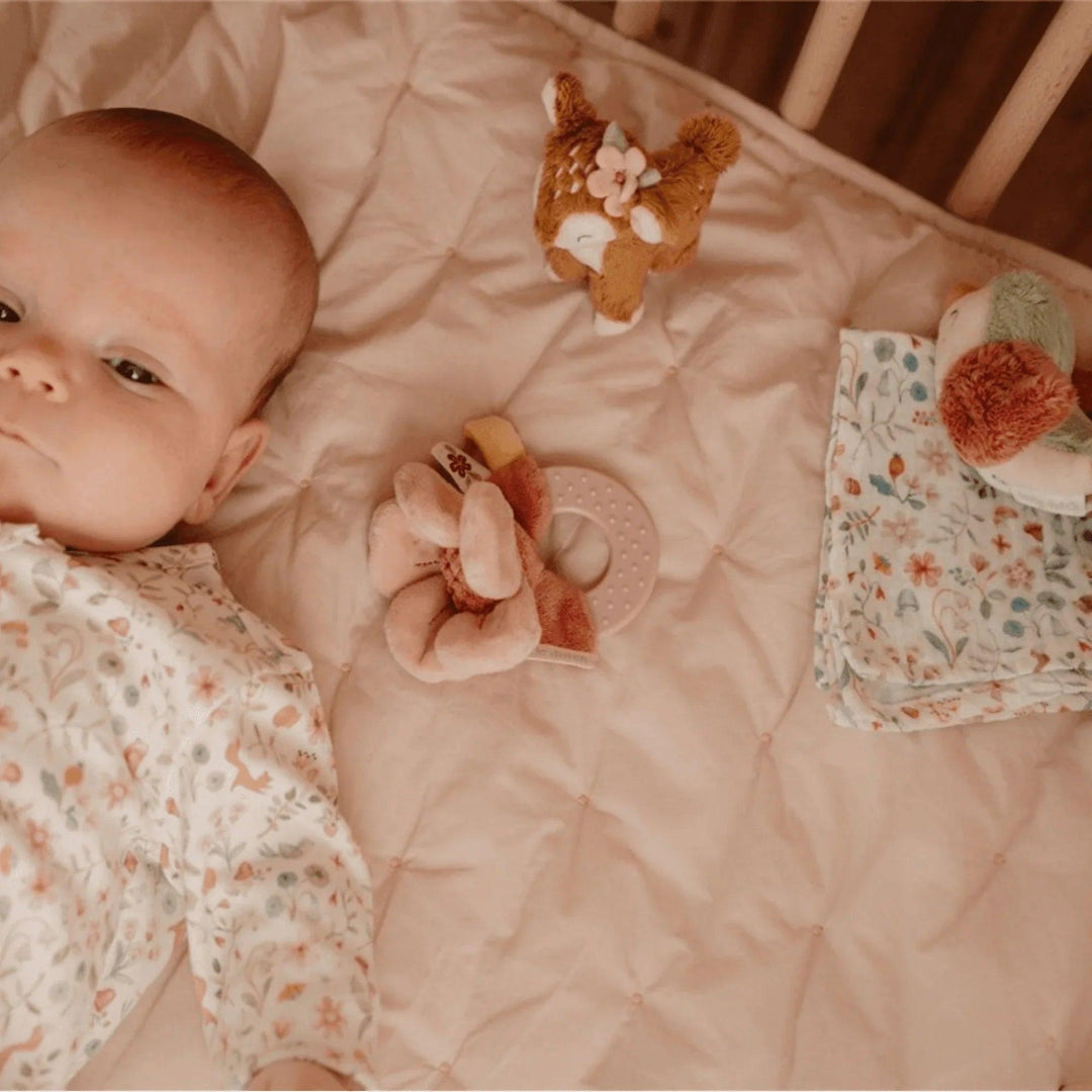 Baby lying in crib next to stuffed deer, blanket and flower teether