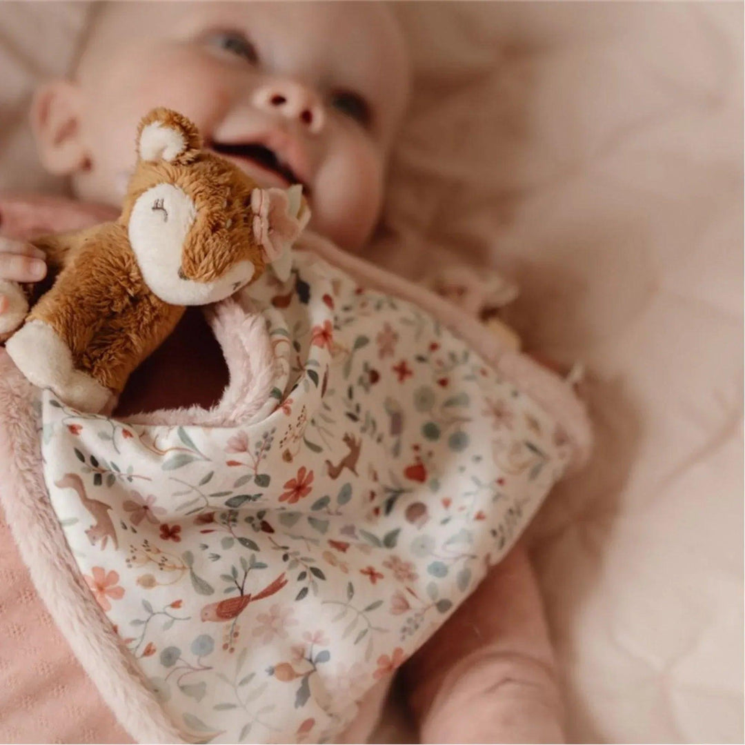 Bébé souriant en jouant avec le dou dou cerf Little Dutch, avec une couverture douce à imprimé floral.