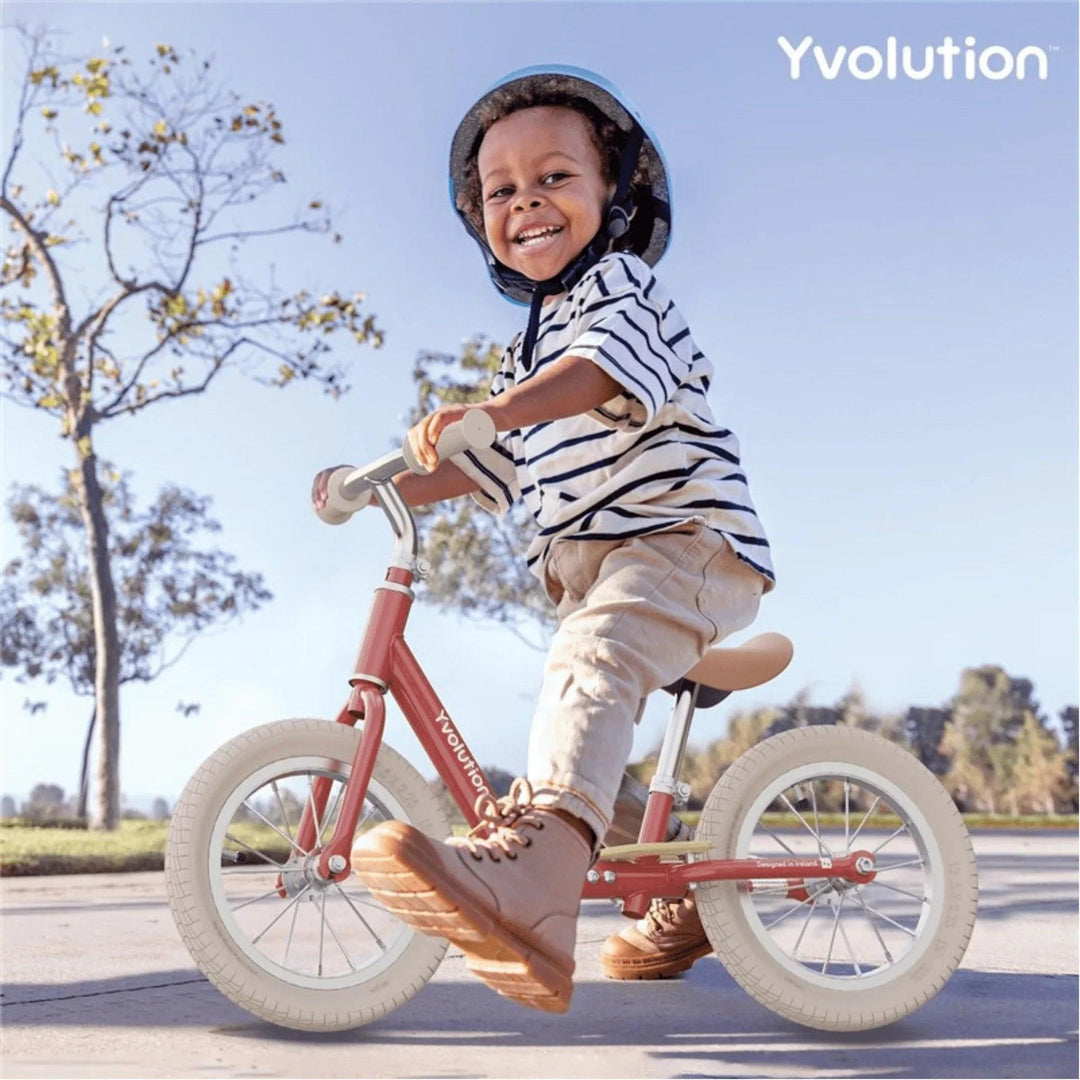 Niño pequeño feliz montando bicicleta sin pedales roja Yvolution al aire libre