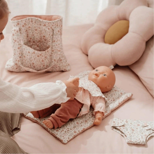 Little girl playing with doll and accessories Little Dutch: handbag, changing mat and floral bib in pink tones