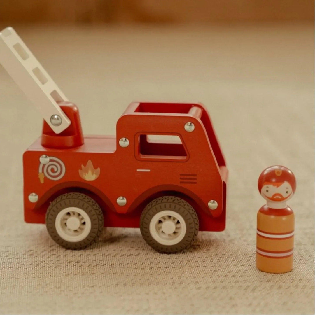 Camion de pompiers en bois rouge avec figurine de pompier jouet Little Dutch sur un tapis beige.