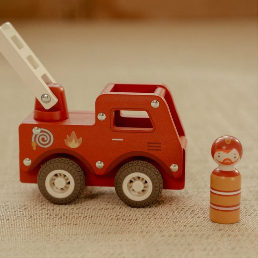 Camión de bomberos de madera color rojo con figura de bombero de juguete Little Dutch sobre una alfombra beige.