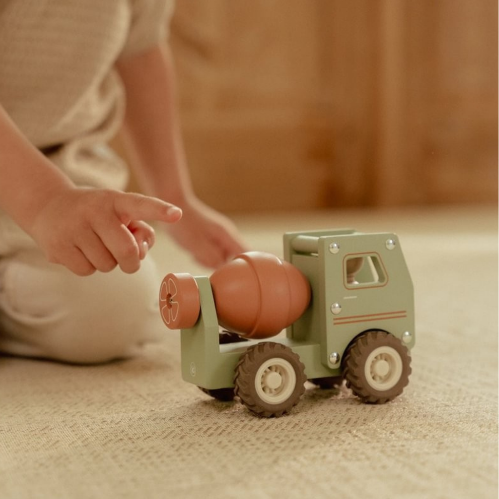Niño pequeño tocando el tambor giratorio de un camión hormigonera de madera Little Dutch sobre una alfombra beige.
