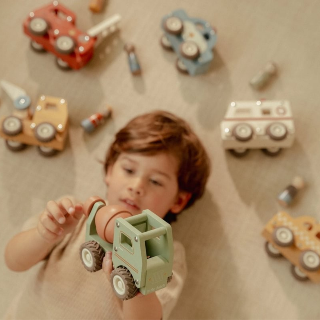 Niño jugando en el suelo con un camión hormigonera de madera Little Dutch rodeado de otros vehículos de juguete.