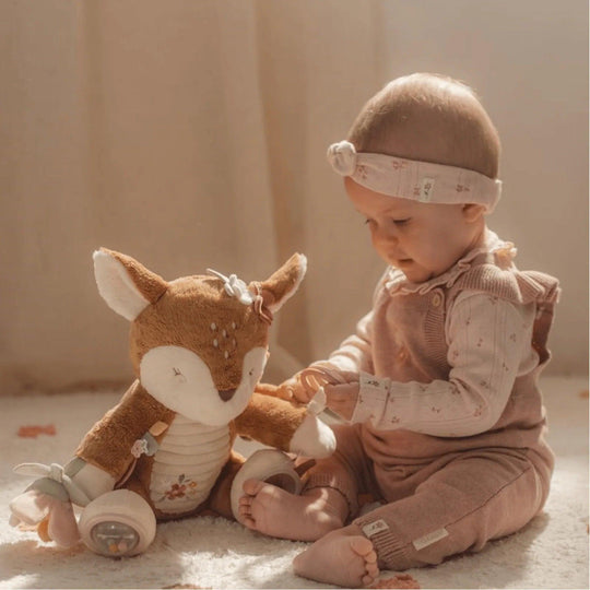 Bébé assis sur le sol interagissant avec une peluche sensorielle en forme de cerf, avec des accessoires éducatifs