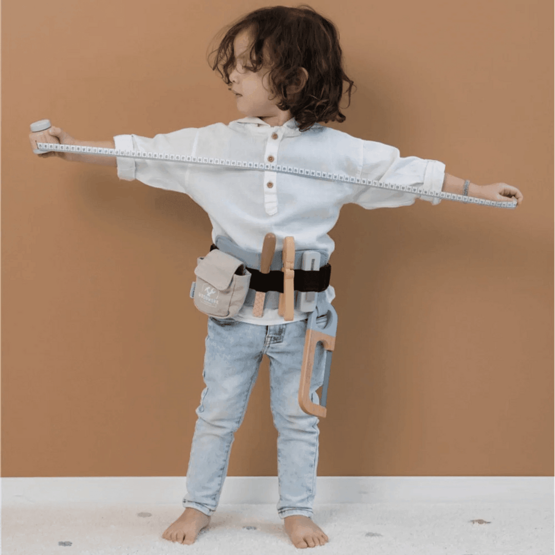 Boy playing with a wooden tool belt, holding a tape measure, ideal for developing motor and creative skills.