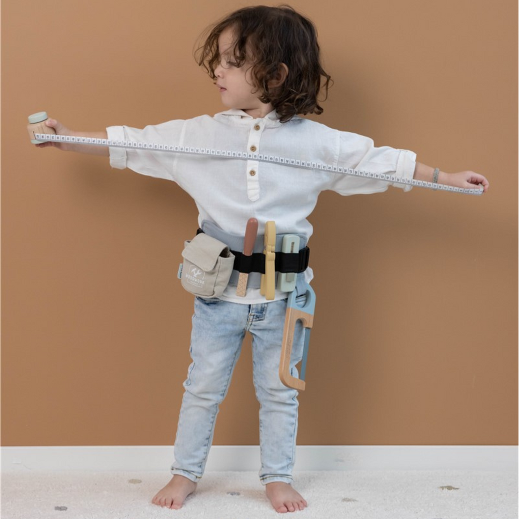 Niño jugando con un cinturón de herramientas de madera, sosteniendo una cinta métrica, ideal para el desarrollo de habilidades motoras y creativas.