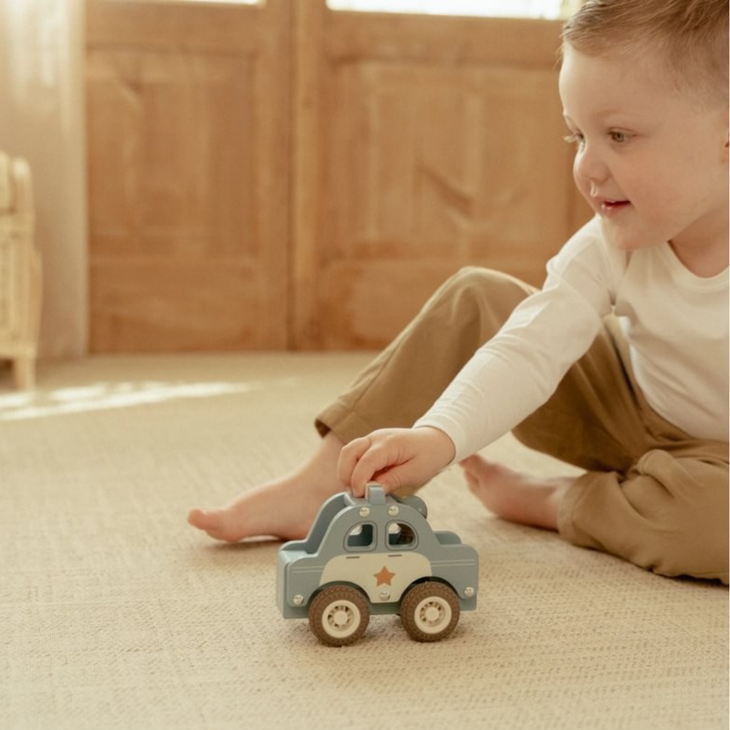 Niño jugando en el suelo con un coche de policía de madera Little Dutch en una habitación luminosa