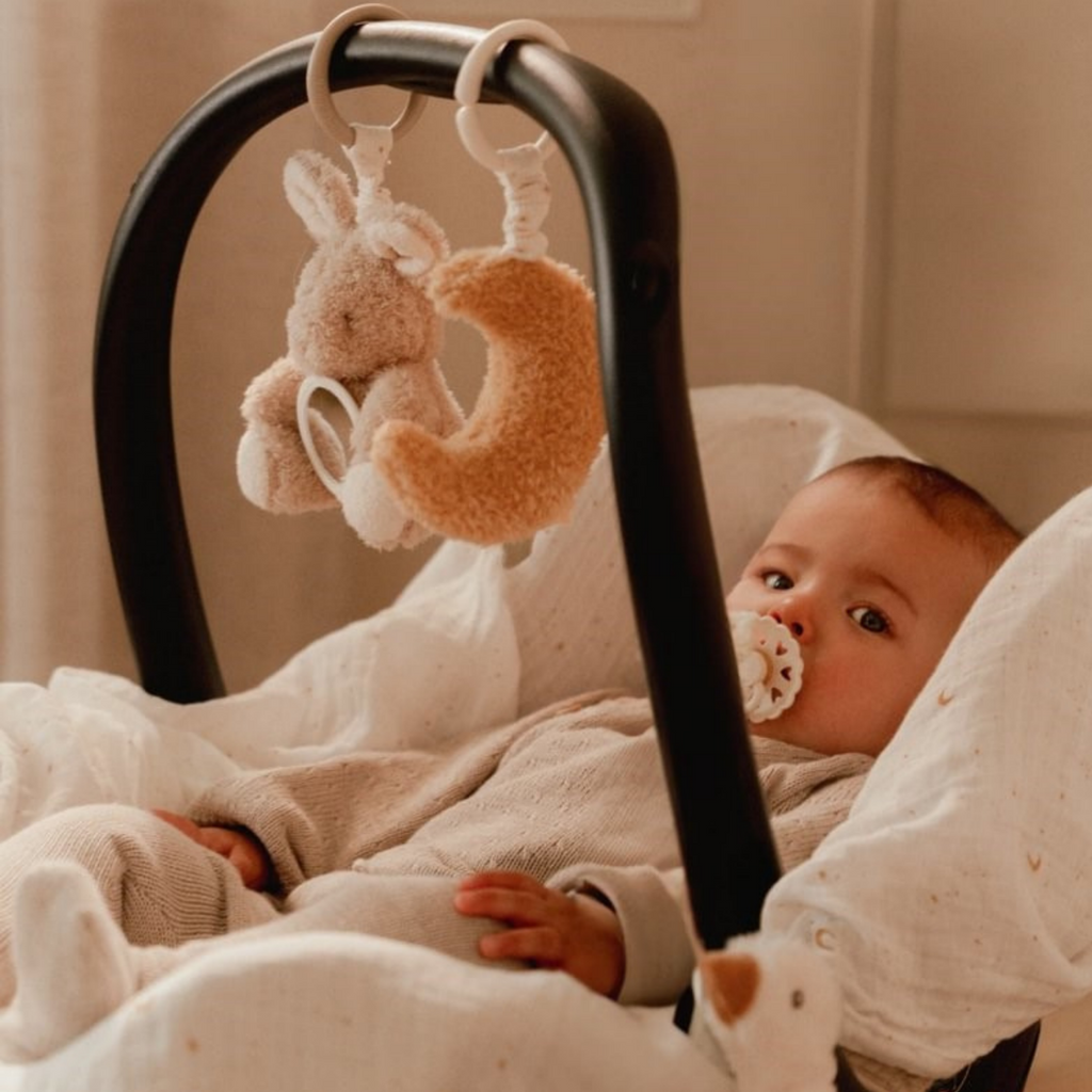 Bebé en portabebés con juguetes colgantes Little Dutch de luna y conejo en tonos neutros