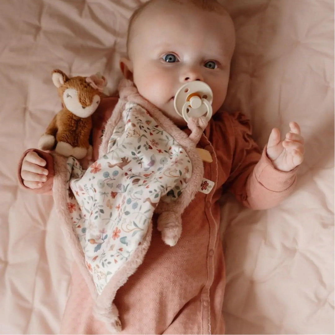 Bébé câlinant le doudou cerf sous une couverture à fleurs roses de la marque Little Dutch, idéal pour apaiser et réconforter bébé.