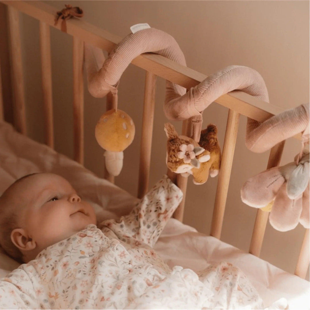 Bebé en cuna mirando espiral de actividades con peluches colgantes: flor, ciervo y seta