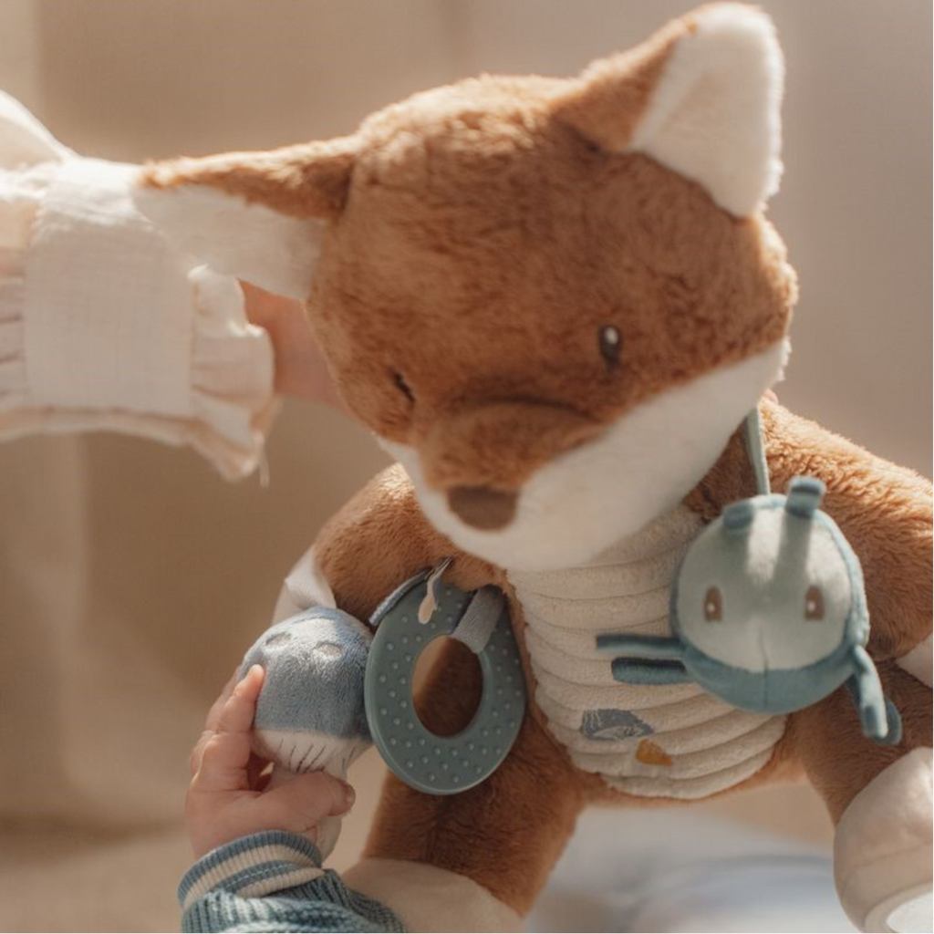 Detalle del peluche zorro sensorial mostrando el bicho azul colgante y accesorios de juego.
