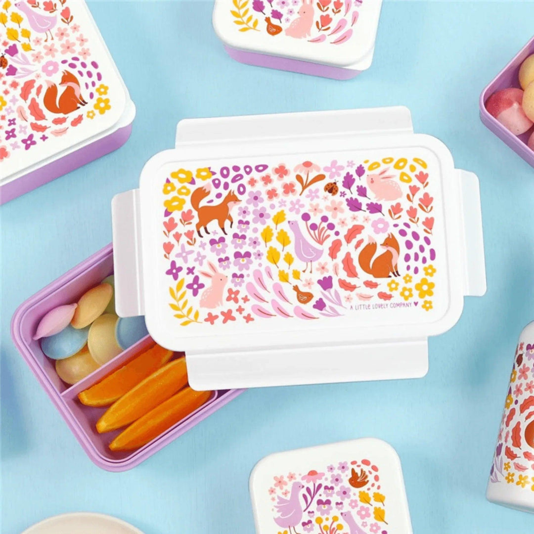 Fiambrera abierta con compartimentos llenos de snacks y dulces, diseño decorativo de bosque encantado