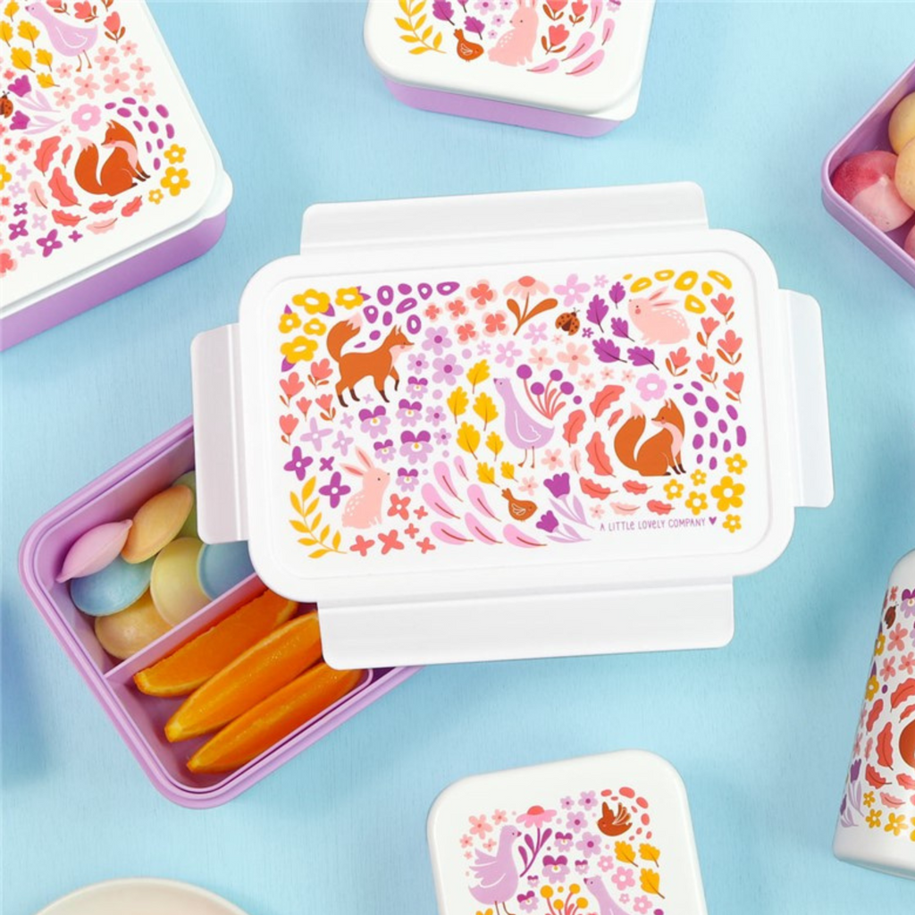 Fiambrera abierta con compartimentos llenos de snacks y dulces, diseño decorativo de bosque encantado