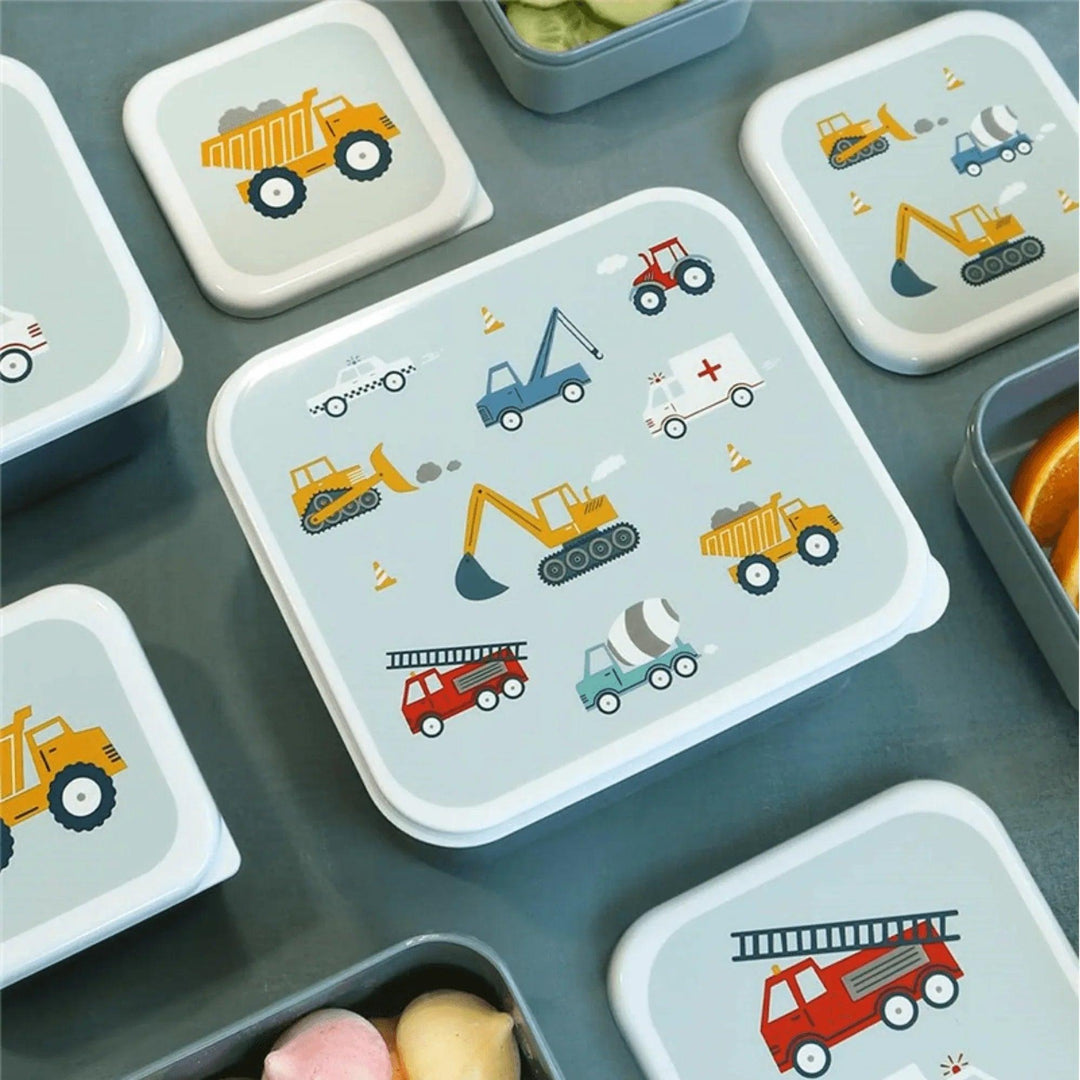 Cajas de almuerzo infantiles abiertas con ilustraciones de camiones, excavadoras y coches sobre fondo azul.