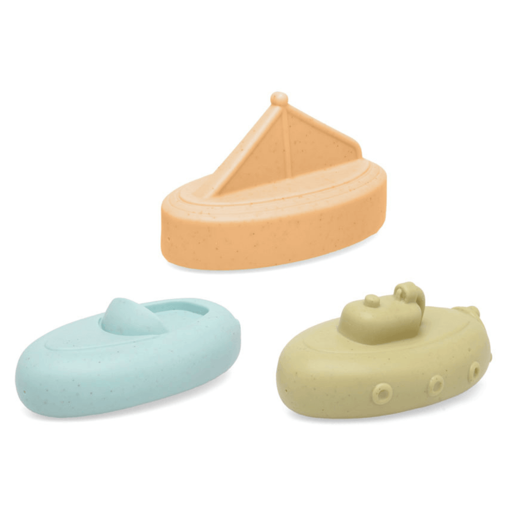 Set de juguetes de baño para bebé en forma de barcos flotantes de silicona en colores pastel sobre una toalla blanca.
