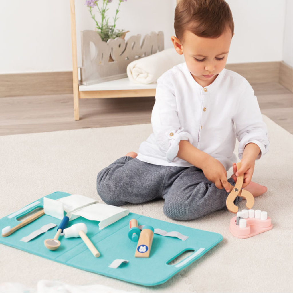 Niño jugando con un kit de dentista de juguete de madera, utilizando las herramientas sobre un modelo de dientes