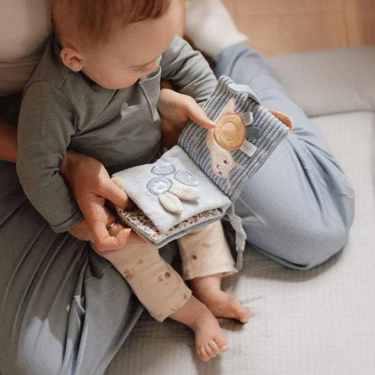 Bébé dans les bras jouant avec un livre sensoriel bleu Little Dutch, pages interactives et activités tactiles