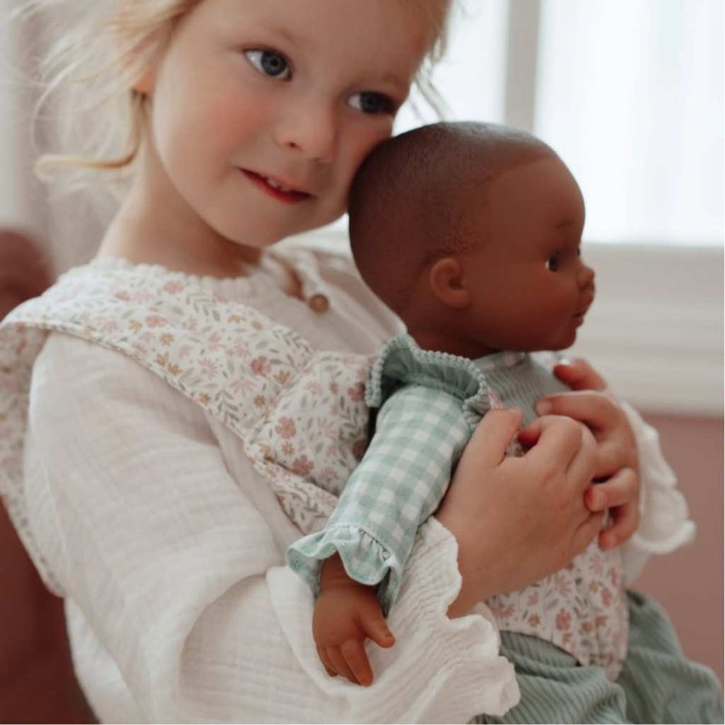 Niña abrazando muñeca en portabebés Little Dutch con estampado floral, en ambiente cálido y acogedor