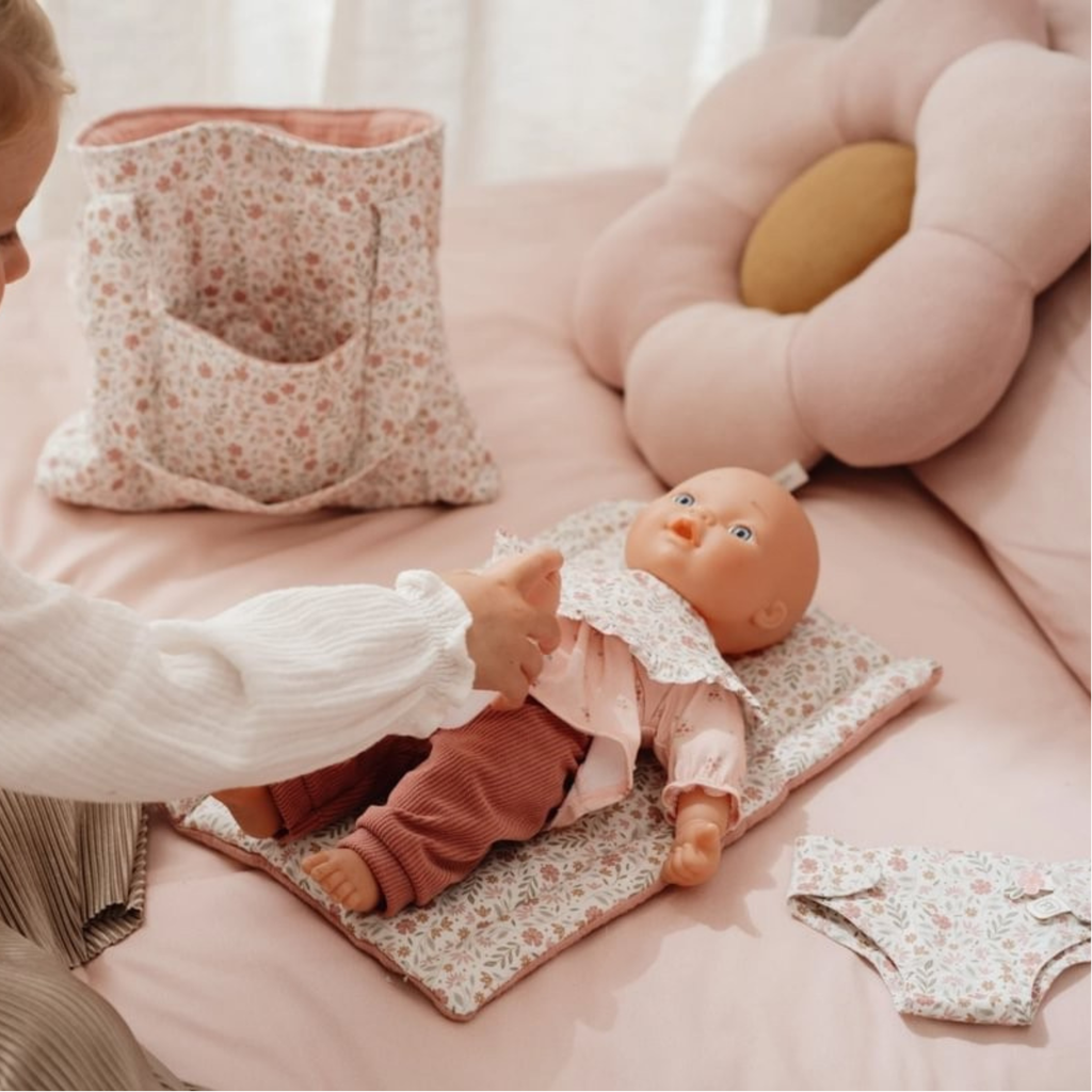 Niña jugando con muñeca y accesorios Little Dutch: bolso, cambiador y babero floral en tonos rosados