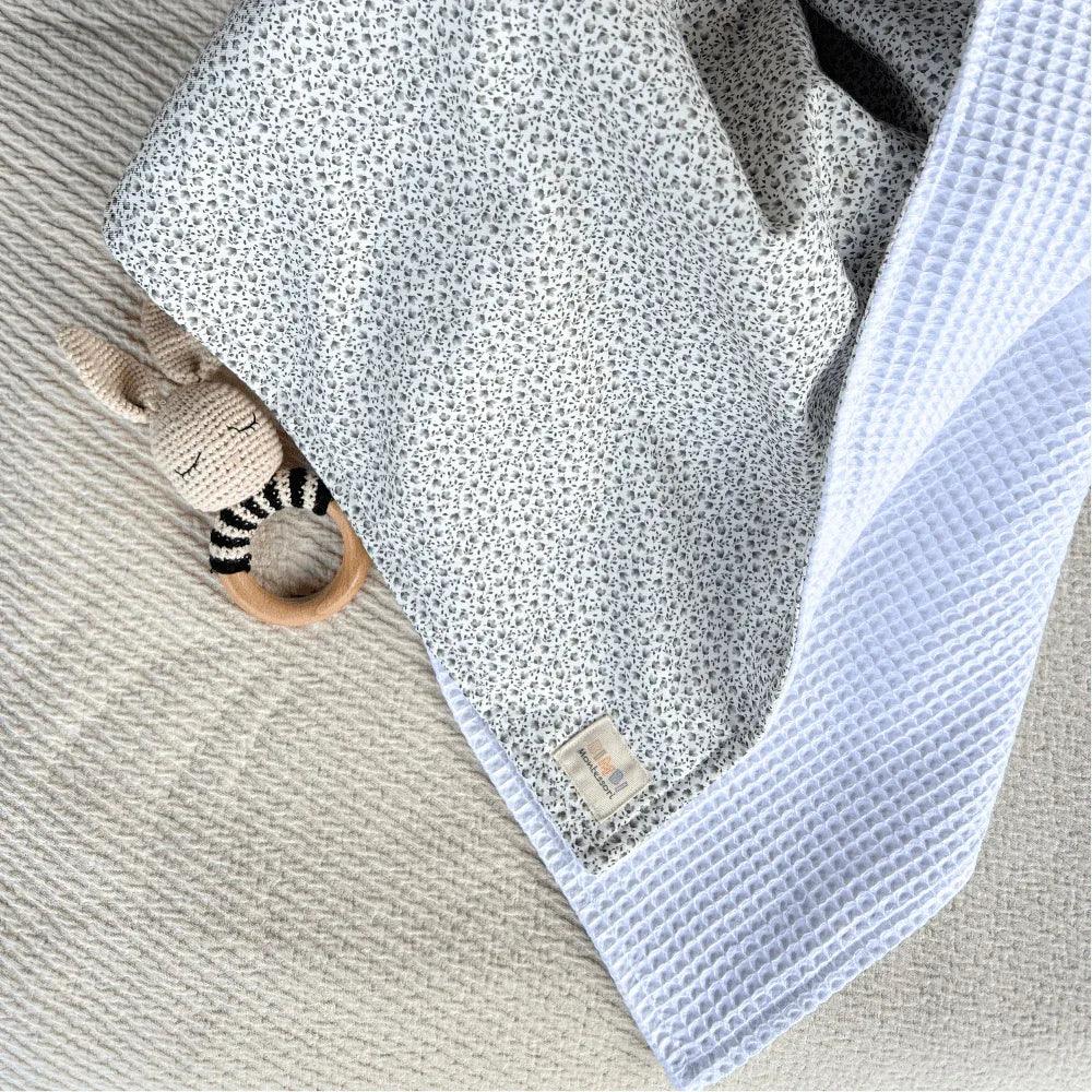 White waffle-textured cotton baby blanket with a gray floral print, a soft and cozy design by Bimbi Montessori.