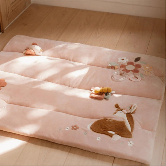 Vue de dessus d'un tapis matelassé rose avec des cerfs, des fleurs, un papillon et des anneaux de dentition pour bébé