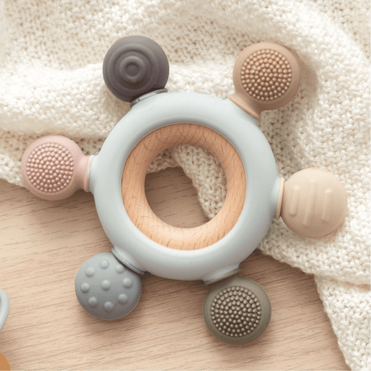 Anneau de dentition pour bébé avec un anneau en bois naturel et des pièces en silicone texturé. Idéal pour soulager les poussées dentaires et stimuler le développement sensoriel.

