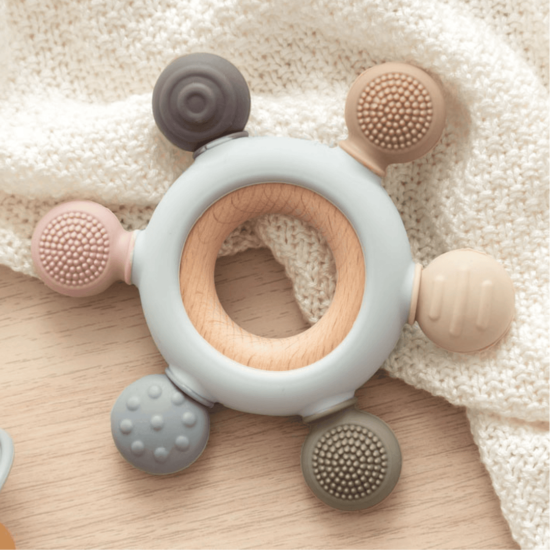 Baby teether with a natural wood ring and textured silicone pieces. Ideal for teething relief and stimulating sensory development.

