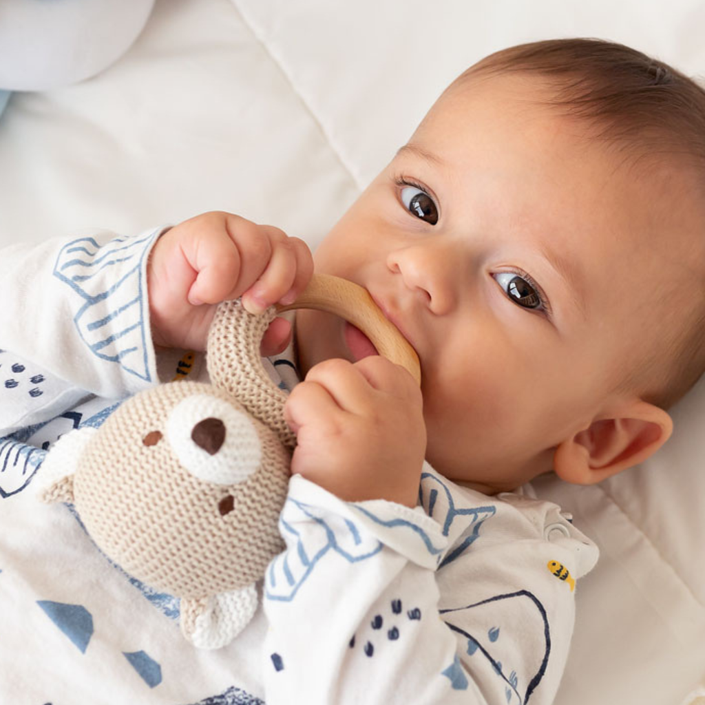 Bebé usando un mordedor de osito tejido con aro de madera natural