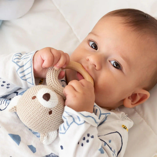 Baby using a knitted teddy bear teether with a natural wooden ring