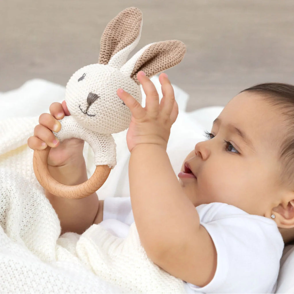 Baby holding a woven rabbit rattle with a wooden hoop, a soft and safe toy