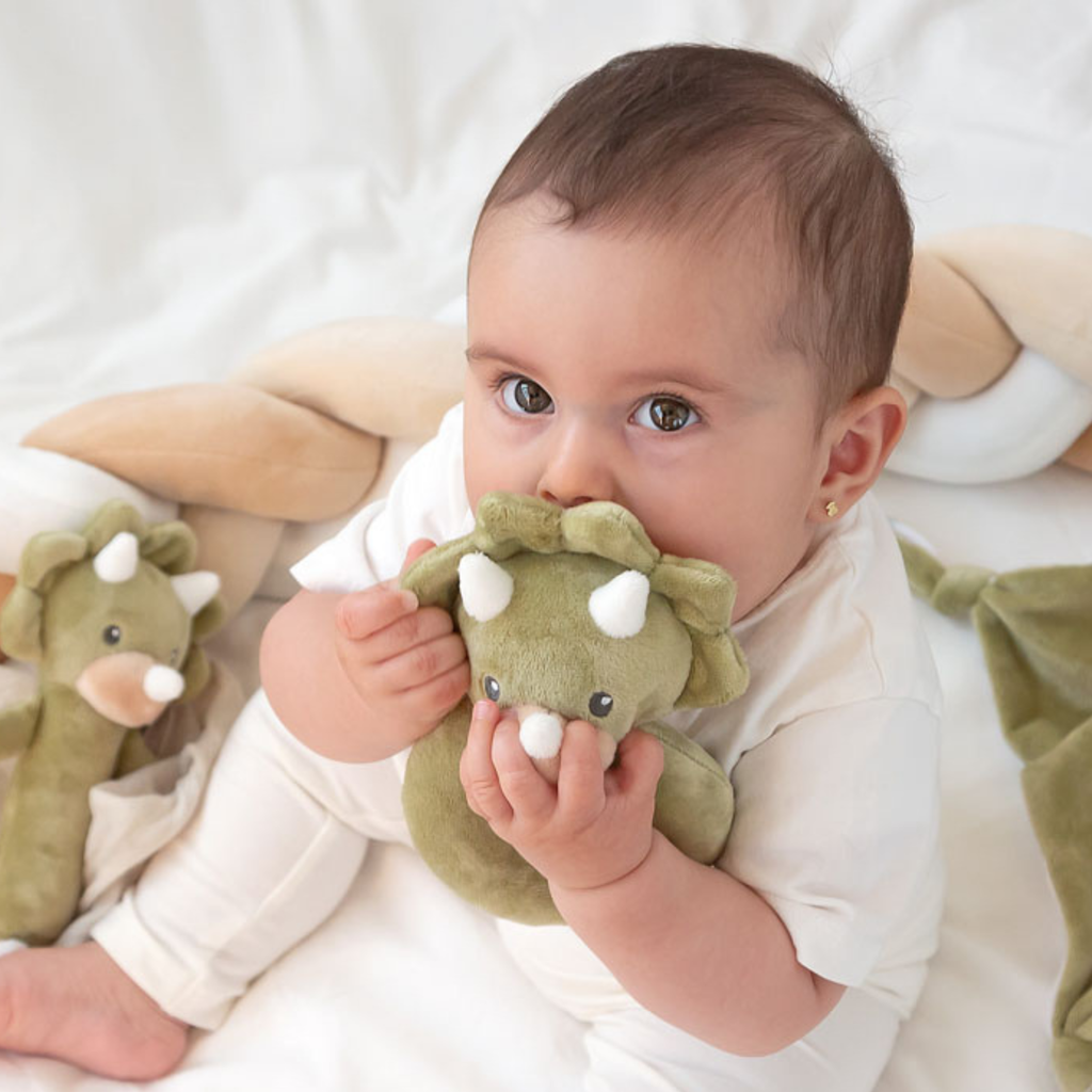 Bebé sosteniendo y mordiendo un mordedor de peluche con forma de dinosaurio triceratops