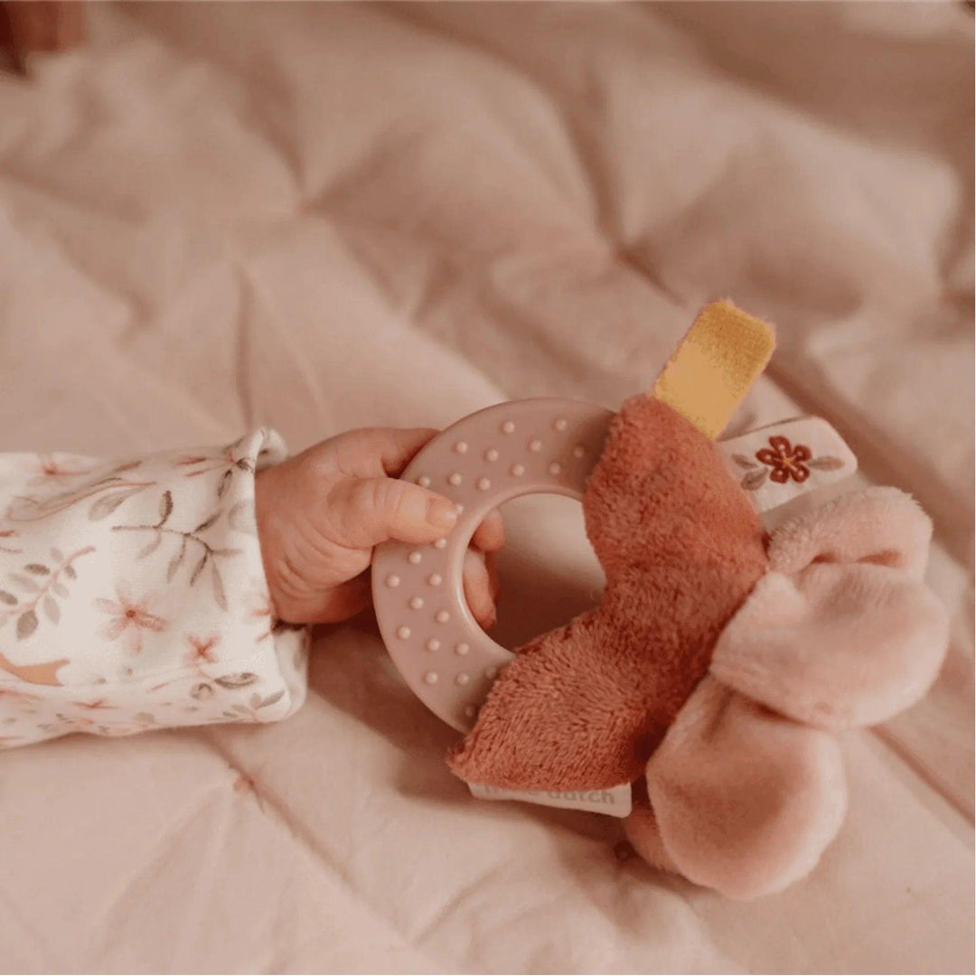 Baby's hand holding a pink teether with a fabric flower, embroidered floral detail