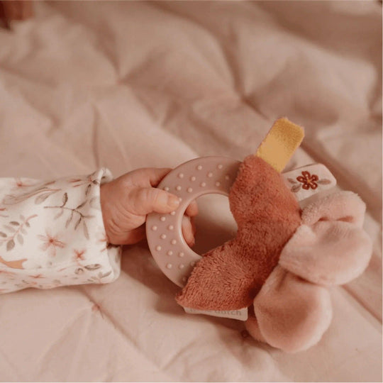 Baby's hand holding a pink teether with a fabric flower, embroidered floral detail