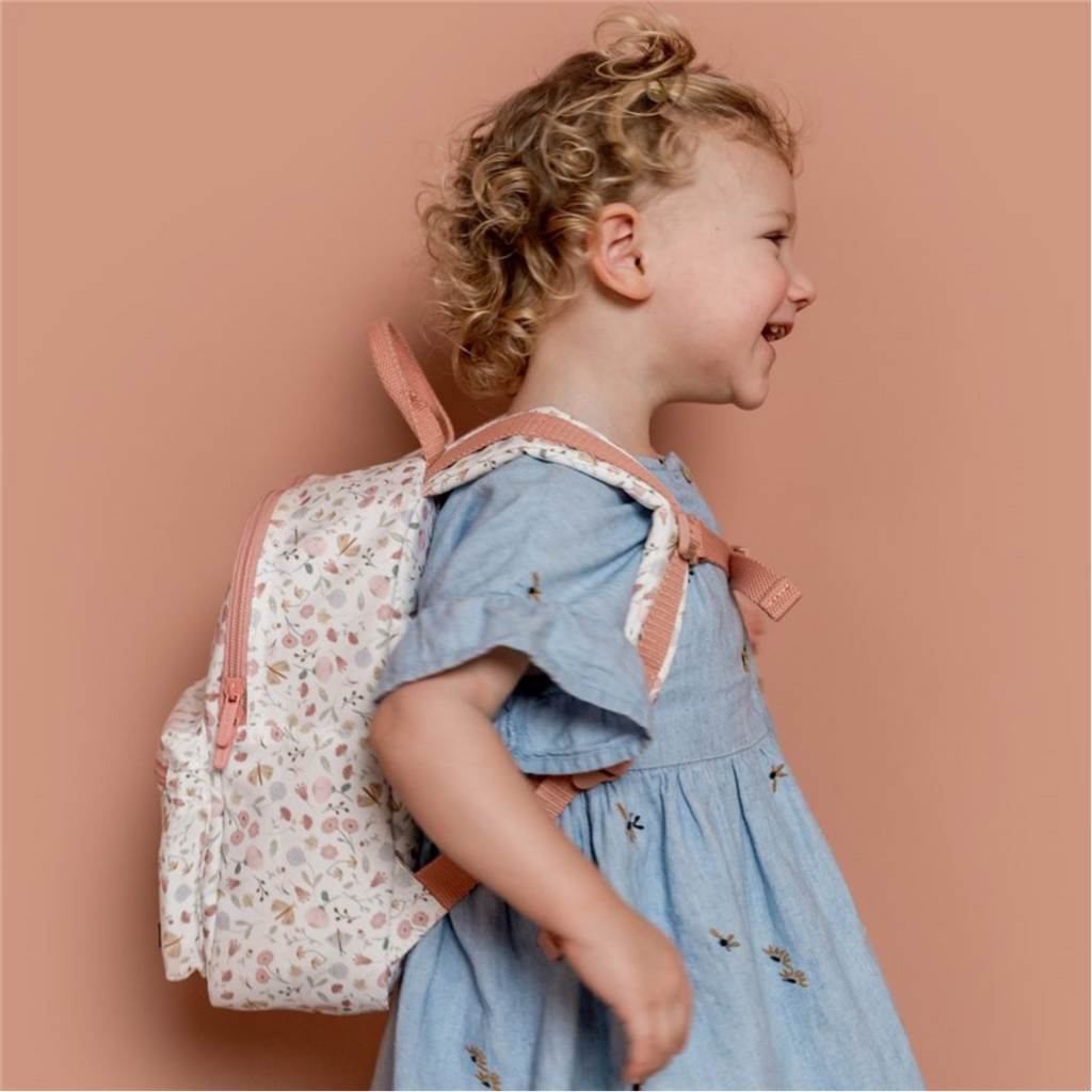 Niña sonriendo con mochila infantil rosa con flores en la espalda