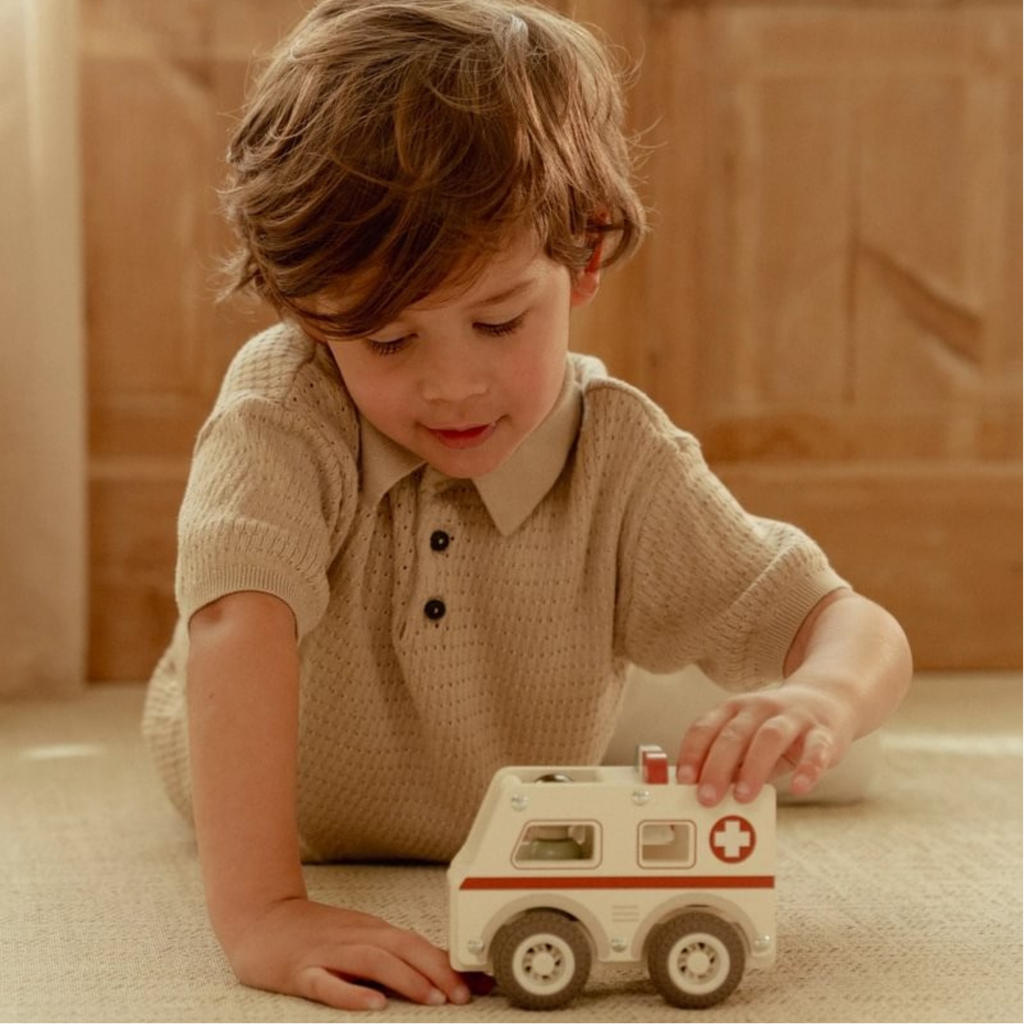 Niño jugando con la ambulancia de madera Little Dutch, fomentando la imaginación y el juego simbólico.
