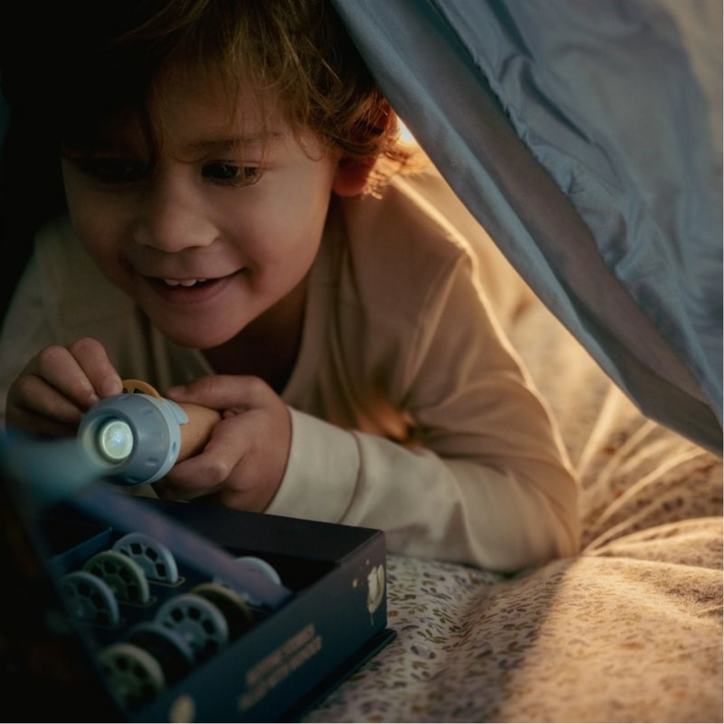 Niño disfrutando de cuentos proyectados con linterna desde la cama, en ambiente nocturno