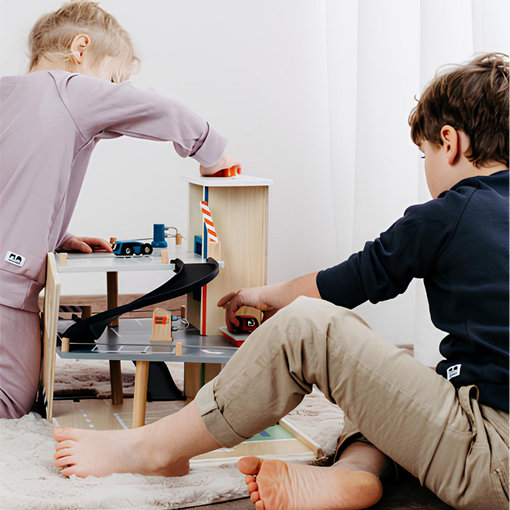 Dos niños jugando con un garaje de estacionamiento de madera con rampas, autos y accesorios, fomentando el juego imaginativo.