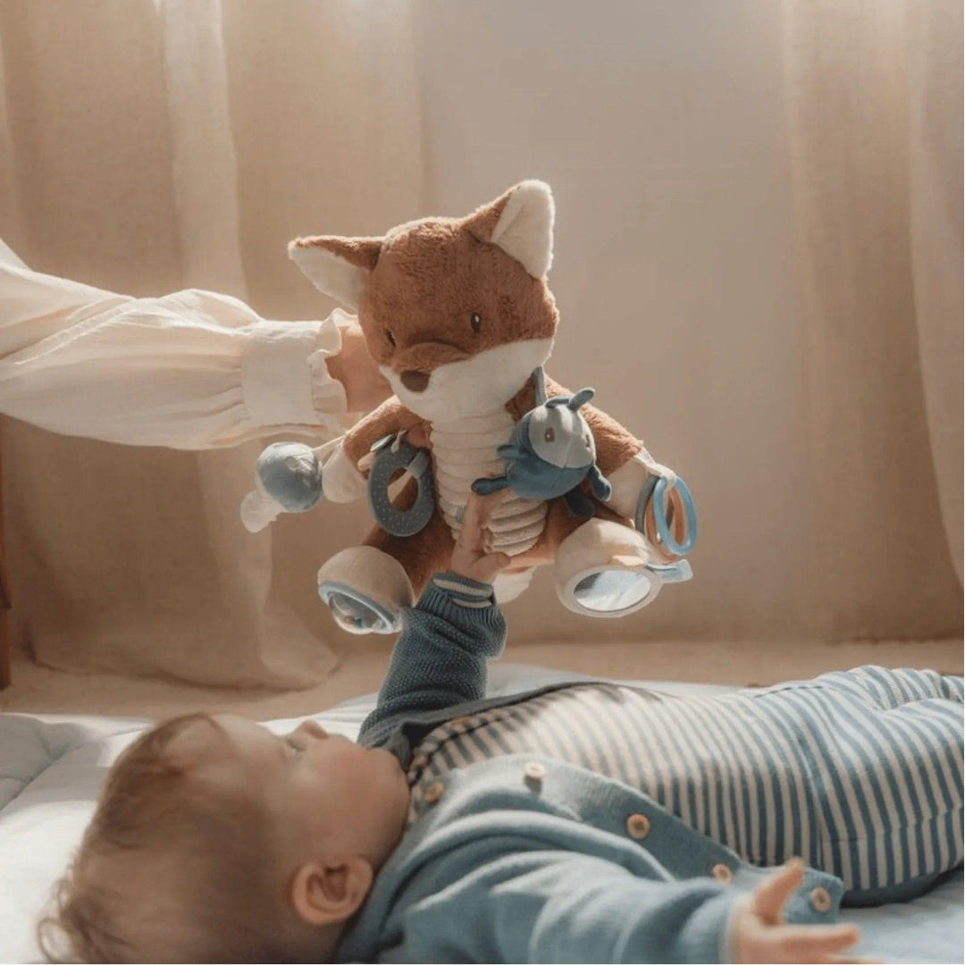 Bambino sdraiato che gioca con una volpe di peluche, stimolazione precoce