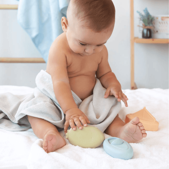Bébé assis jouant avec des jouets de bain en silicone en forme de bateau sur une surface douce.