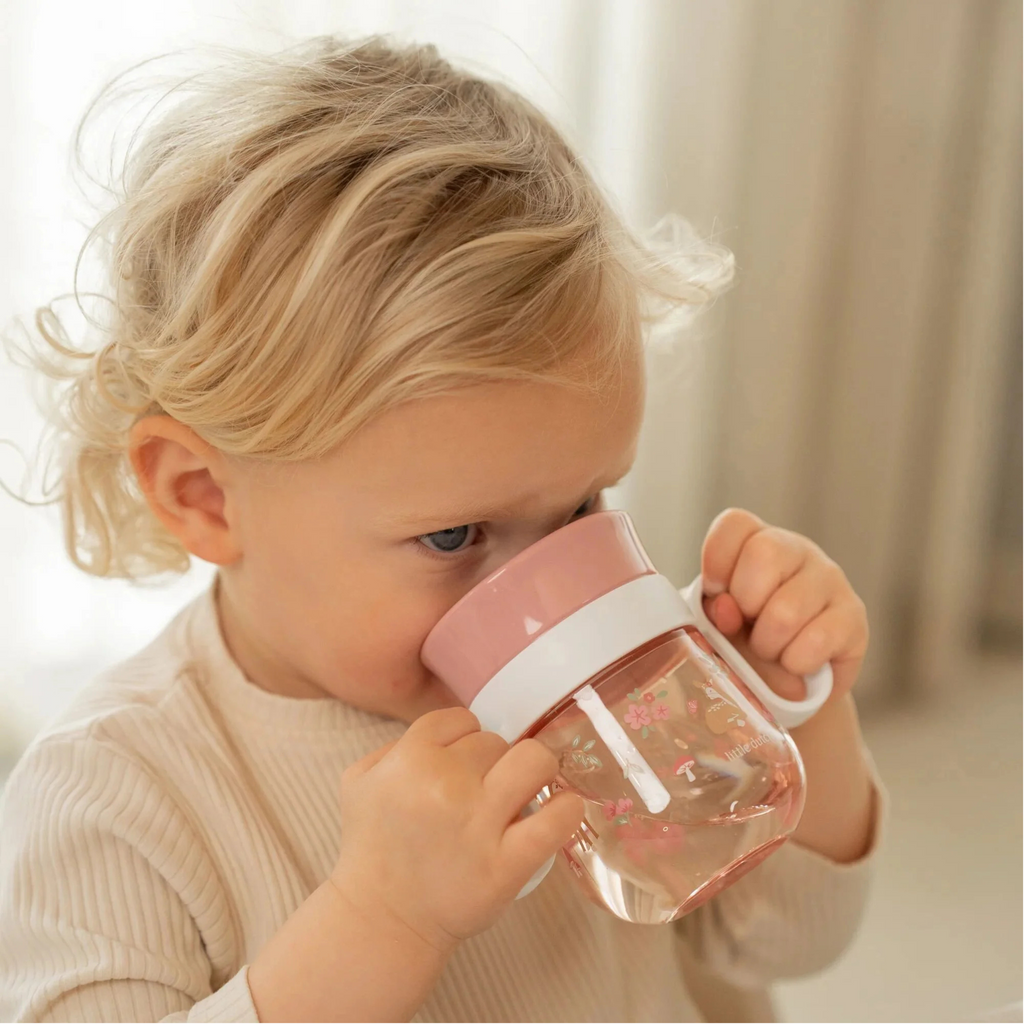 Niña pequeña bebiendo de taza de transición rosada libre de BPA con diseño floral