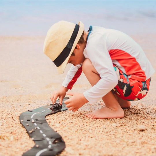 Un enfant joue avec un circuit routier Waytoplay sur la plage avec une voiture miniature