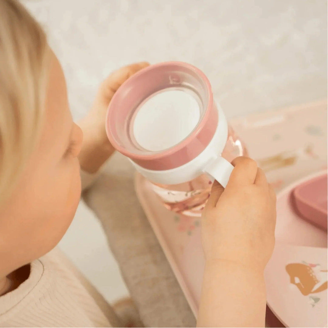 Niña sujetando vaso de aprendizaje rosado con diseño de flores y asas blancas
