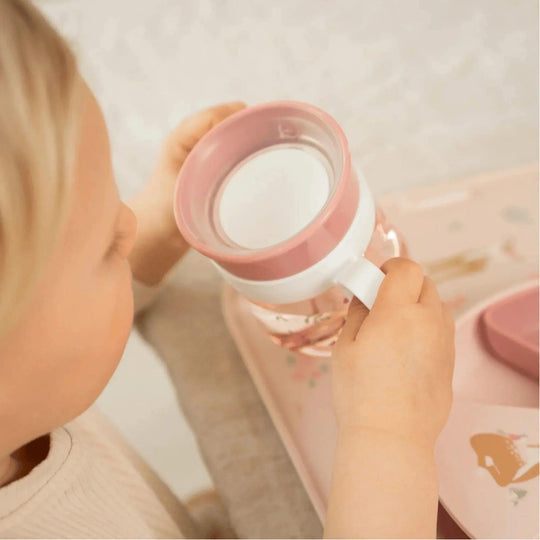 Petite fille tenant une tasse rose avec un motif de fleurs et des poignées blanches