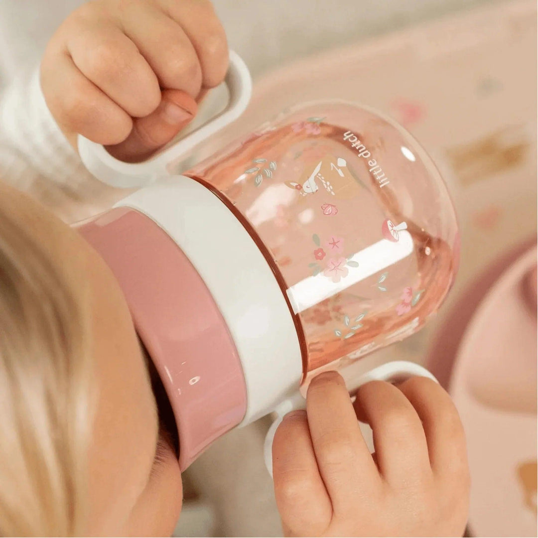 Detalle de vaso de bebé antigoteo con asas y decoración floral rosada sobre bandeja