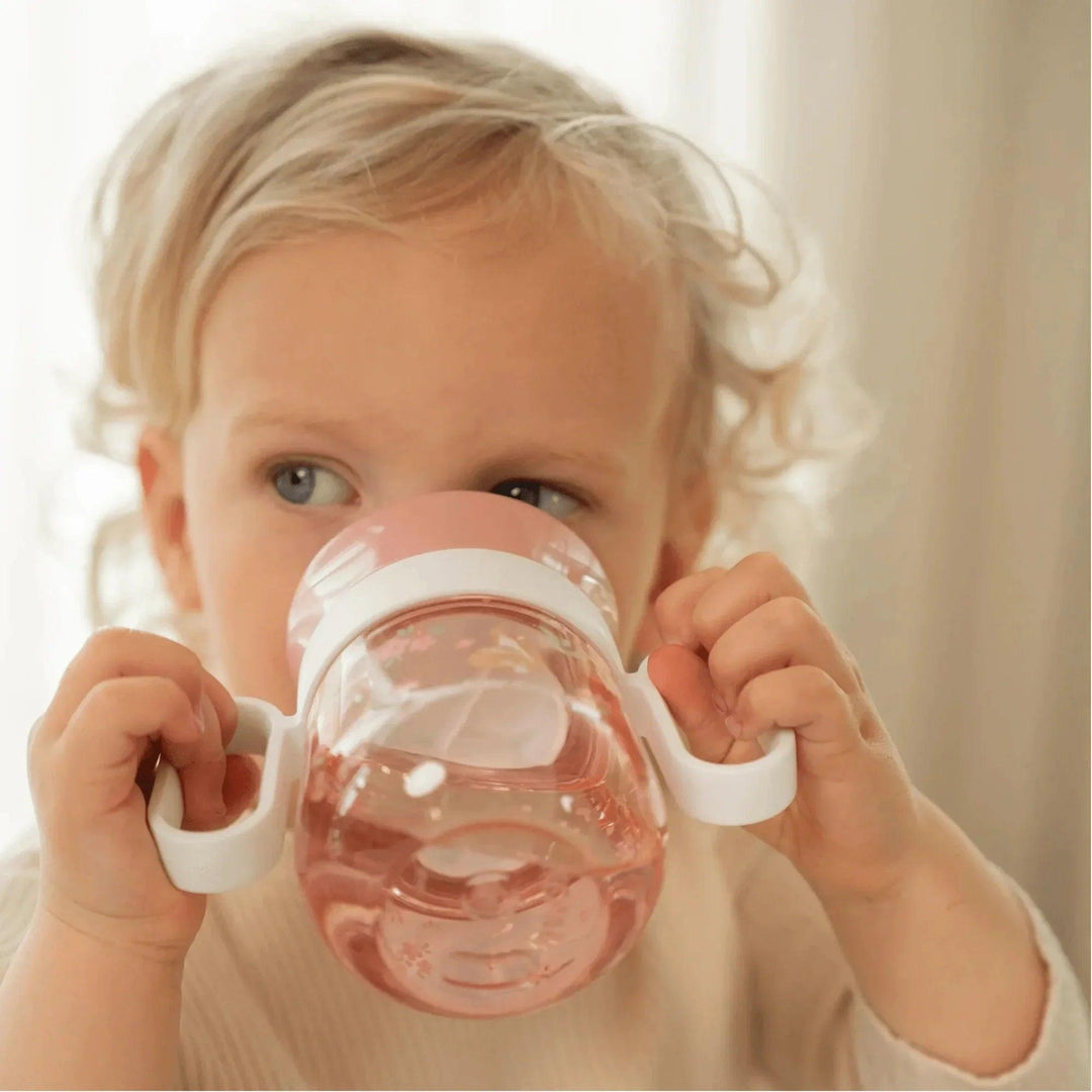 Bebé usando vaso de entrenamiento antiderrame rosado con asas laterales