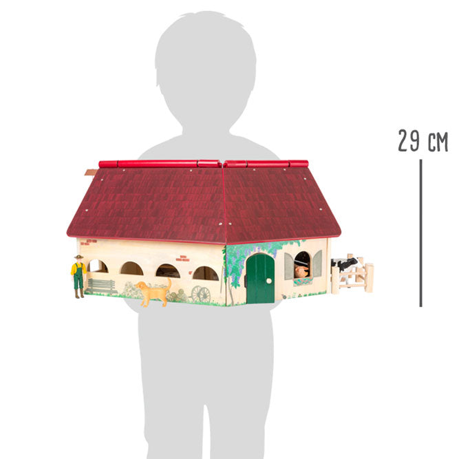 La construcción de madera de la granja juguete está dispuesta en forma de ángulo  y equipada con un techo plegable. Proporción con figura niño. El juguete mide 29 cm de altura